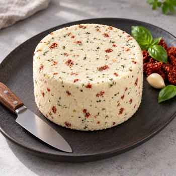 Niewędzony ser z czosnkiem, pomidorem i bazylią 2,5 kg na ciemnym talerzu z dodatkami i nożem.